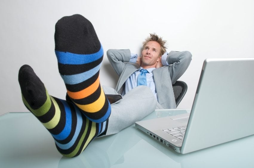 Man with shoes off relaxing at his desk with a laptop.